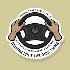 May include: A black and white sticker with a cartoon illustration of a steering wheel and hands holding it. The text on the sticker reads "No I don't know how to drive. Not everybody knows how to do everything. Driving isn't the only thing."