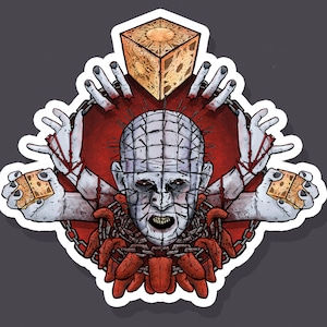 Puede incluir: Una pegatina con una ilustración roja y blanca de un personaje de la película de terror Hellraiser. El personaje tiene una cadena con ganchos alrededor del cuello y sostiene una pequeña caja en forma de cubo en cada mano. La caja es de color dorado con un diseño rojo y blanco.