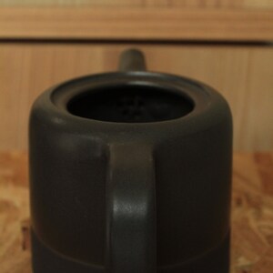 May include: A black ceramic teapot with a round body and a single handle. The teapot has a strainer inside the spout.