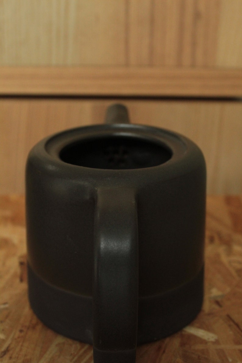 May include: A black ceramic teapot with a round body and a single handle. The teapot has a strainer inside the spout.