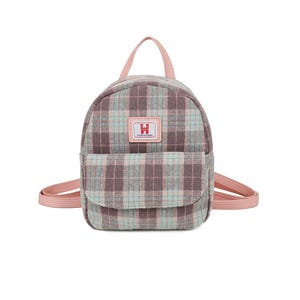 May include: A small backpack with a plaid pattern in shades of brown, pink, and blue. The backpack has a front pocket, a top handle, and adjustable shoulder straps, all in a soft pink colour. A small rectangular patch with the letter "H" is on the front.