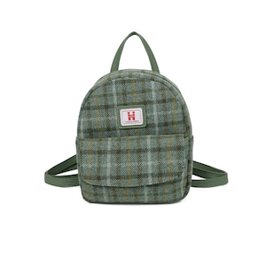 May include: A small, green plaid backpack with a top handle and adjustable straps. The backpack has a front pocket and a small rectangular patch with a logo. The bag is made of a textured fabric.