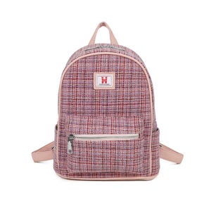 May include: Pink tweed backpack with a front zipped pocket and side pockets. The backpack has a top handle and adjustable shoulder straps. A small rectangular patch with the letter "H" is on the front.