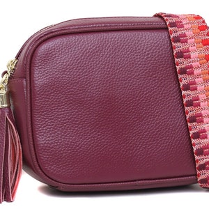 Sac en cuir pour femme style sac photo bandoulière avec pommades en cuir sur les fermetures éclair et bandoulière en toile réglable. La couleur est bordeaux.
