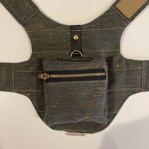 Pode incluir: Um arn&ecirc;s para c&atilde;o de lona verde escuro com um pequeno bolso com z&iacute;per e um anel de metal dourado. O arn&ecirc;s tem uma al&ccedil;a de couro marrom e um bot&atilde;o de metal dourado. O texto "FABQUILTBBYFAISAL" est&aacute; impresso na parte inferior da imagem.