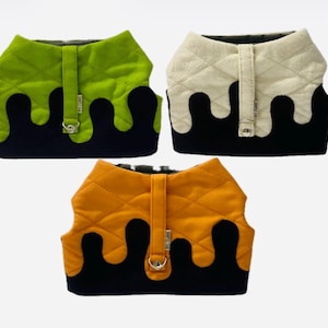 May include: Three quilted pet harnesses featuring a black base with a dripping paint design in lime green, cream, and orange. Each harness includes a vertical center strap with a silver metal D-ring and a small rectangular tag labeled Simply Fab.