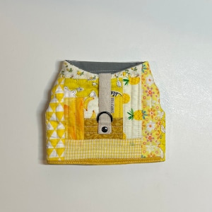 Pode incluir: Colete acolchoado para cão amarelo e branco com uma etiqueta "SIMPLY FAB" e um anel D de metal.