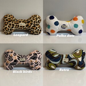 May include: Four dog bone-shaped toys with different patterns. One has a leopard print, another has polka dots, a third features black birds on a pink background, and the last has a retro design. Each toy has a "SIMPLY FAB" label.