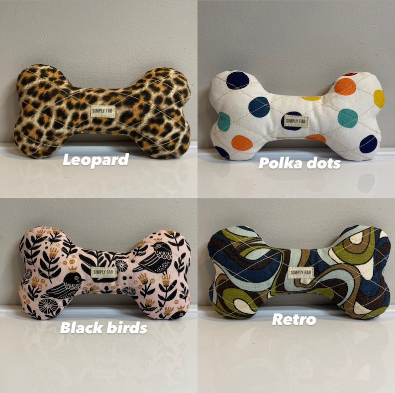 May include: Four dog bone-shaped toys with different patterns. One has a leopard print, another has polka dots, a third features black birds on a pink background, and the last has a retro design. Each toy has a "SIMPLY FAB" label.