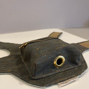 Pode incluir: Um arn&ecirc;s para c&atilde;o em lona cinzento escuro com um pequeno bolso com fecho de correr e um anel de metal dourado. O arn&ecirc;s tem uma guarni&ccedil;&atilde;o azul claro e um r&oacute;tulo castanho que diz "FABQUALITYBYFAISAL".