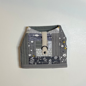 May include: A gray quilted dog harness with a floral and fish print. The harness has a white strap with a black buckle and the text "SIMPLY FAB" printed on it.