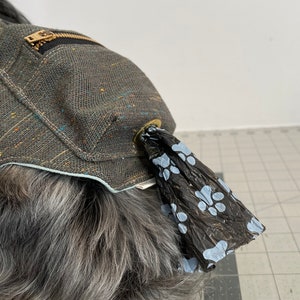 Pode incluir: Um porta-sacos para excrementos de c&atilde;es de lona cinza com um bolso com z&iacute;per e um design de pegada de pata azul. O porta-sacos est&aacute; preso ao colar de um c&atilde;o.