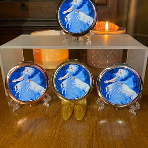 Peut inclure: Trois miroirs de poche avec une image bleue et blanche d'une femme et d'un chien blanc. Les miroirs sont sur des supports avec des finitions dorées, argentées et or rose.