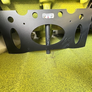 May include: Black plastic mounting plate with multiple holes and a large oval cutout. The plate is designed to be mounted to a surface and has a black metal rod extending from the centre.