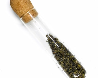 May include: A glass test tube with a cork stopper filled with dried green herbs.
