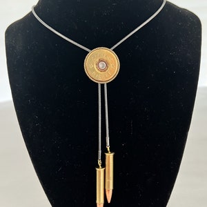 May include: A silver chain bolo tie with a gold shotgun shell pendant and two gold bullet charms.