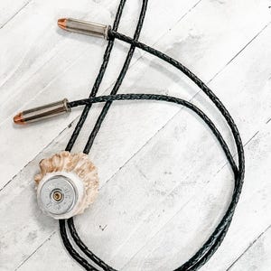 May include: A black braided bolo tie with a silver bullet casing and a piece of antler attached to the end.