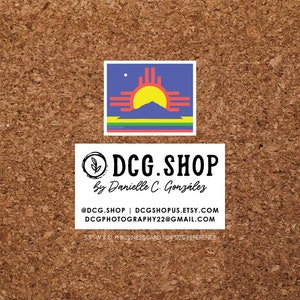 May include: A business card with a white background and black text. The text reads "DCG.SHOP by Danielle C. González @DCG.SHOP | DCGSHOPUS.ETSY.COM DCGPHOTOGRAPHY22@GMAIL.COM 3.5 W X 2 H BUSINESS CARD FOR SIZE REFERENCE". The card also features a small image of the New Mexico state flag.