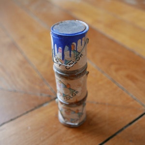 Peut inclure: Une pile de trois petits pots de peinture avec des étiquettes colorées. Le pot du haut est ouvert et de la peinture bleue coule sur le côté. Les étiquettes sur les pots disent "My Color".