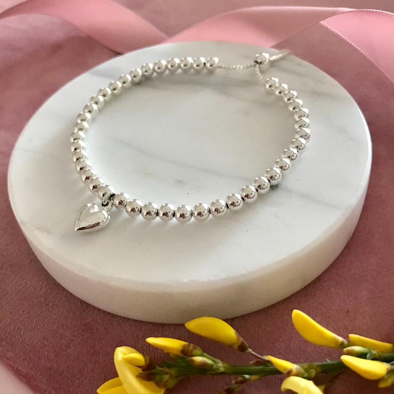 May include: A silver bracelet with a heart charm. The bracelet is made of small, round beads and has a sliding clasp.