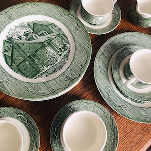 Może przedstawiać: Zestaw vintage porcelanowej zastawy stołowej w kolorze zielonym i białym z motywem wiejskiego domu. Zestaw zawiera talerze, spodki i filiżanki do herbaty.