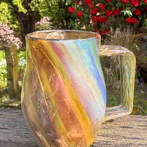 May include: A clear glass mug with a rainbow iridescent swirl design. The mug has a rounded body and a handle.