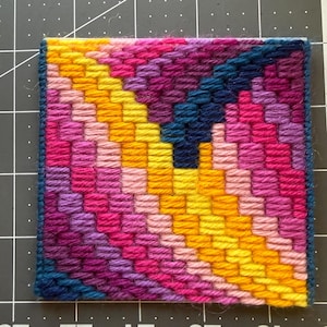Könnte beinhalten: Ein kleines, rechteckiges Gobelin-Stück mit einem lebendigen, geometrischen Design. Das Kunstwerk zeigt ein Farbspektrum, darunter Gelb, Rosa, Lila und Blau, das in einem diagonalen Muster angeordnet ist. Die Kanten sind mit einem dunkelblauen Rand versehen.
