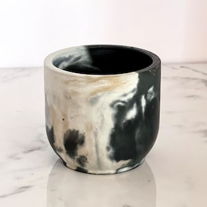 May include: A small, black and white marbled ceramic planter. The planter has a rounded shape and a smooth, matte finish.