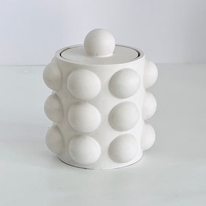 May include: White ceramic jar with a lid. The jar has a textured surface with a pattern of raised circles.