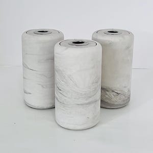 May include: Three white cylindrical ceramic vases with a marbled pattern and silver tops.