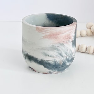 May include: A small, round, concrete planter with a marbled design in shades of white, gray, and pink.