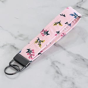 May include: A pink fabric key chain with a floral pattern and a silver key ring.