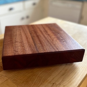 May include: A large, rectangular, wooden cutting board with a rich reddish-brown color. The board has a smooth, polished surface and a slightly raised edge.