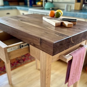 May include: A wooden kitchen island with a walnut countertop, a drawer, and a towel rack. The island is made of light wood and has a natural finish.