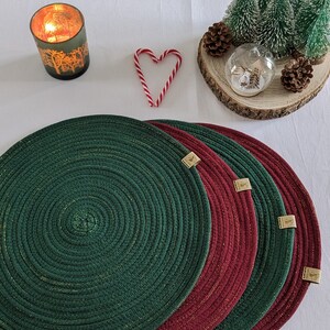 May include: Four round placemats, two green and two burgundy, with gold thread woven into the fabric. The placemats are stacked on top of each other.