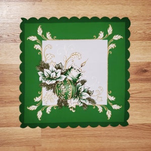 May include: Green table runner with a scalloped edge and a white center featuring a gold and green Christmas ornament with floral accents.