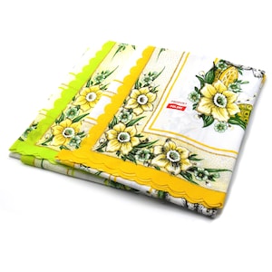 May include: Folded white tablecloth with a floral pattern featuring yellow daffodils and green leaves. The tablecloth has a scalloped yellow border and a green border. The text "PRODUKT POLSKI" is visible on a red label.