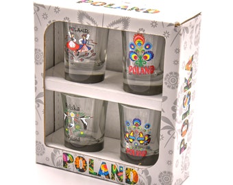 Puede incluir: Conjunto de cuatro vasos de chupito en una caja. Cada vaso presenta un diseño diferente de arte popular polaco, incluyendo una pareja bailando, un patrón floral, una cigüeña y un gallo. La caja es blanca con la palabra "POLAND" impresa en letras de colores.