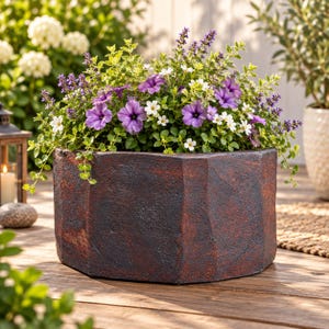 May include: A hexagonal planter with a dark, textured, rust-colored finish containing a vibrant arrangement of purple petunias, small white flowers, and green foliage. The container features a faceted, stone-like appearance with deep brown tones.