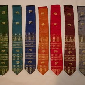 May include: A collection of nine silk neckties in various colors, including green, blue, orange, and red. Each tie features a repeating gold elephant motif and geometric patterns. The ties are displayed side by side.
