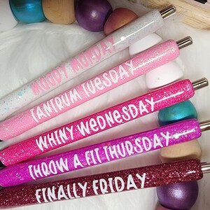 May include: Five glitter pens with different colored glitter and white text. The text on the pens reads "Moody Monday", "Tantrum Tuesday", "Whiny Wednesday", "Throw a Fit Thursday", and "Finally Friday".