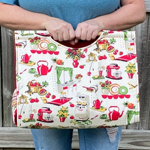 Può includere: Una borsa tote in tela bianca con un manico rosso e un bordo rosso. La borsa è decorata con una stampa da cucina vintage con mele rosse, un frullatore rosso, una teiera rossa e altri oggetti da cucina.