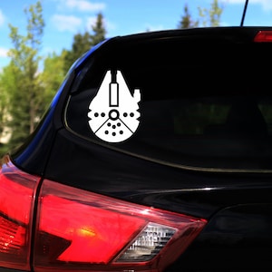 Può includere: Un'auto nera con un adesivo bianco del Millennium Falcon sul lunotto posteriore.