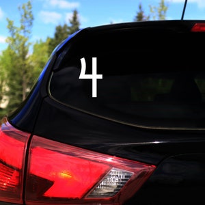 Op de afbeelding: Een zwarte auto met een witte sticker van het symbool voor de planeet Jupiter op de achterruit.