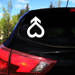 Op de afbeelding: Een zwarte auto met een witte hart- en pijl sticker op de achterruit.