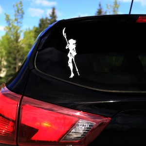 Op de afbeelding: Een zwarte auto met een witte vinyl sticker van een vrouw die een staf vasthoudt op het achterraam.