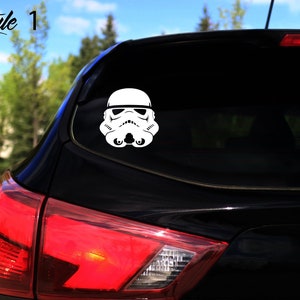 May include: A white vinyl sticker of a Star Wars Stormtrooper helmet on the rear window of a black car.