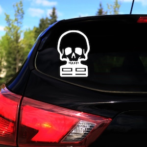 Puede incluir: Un coche negro con una pegatina de calavera y huesos cruzados blancos en la ventana trasera.