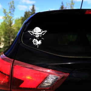 May include: A black car with a white vinyl sticker of Yoda wearing sunglasses and headphones on the rear window.