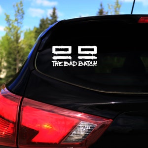 Puede incluir: Un coche negro con una calcomanía blanca en la ventana trasera. La calcomanía dice "The Bad Batch" y presenta dos cuadrados blancos con una línea blanca en la parte superior de cada cuadrado.